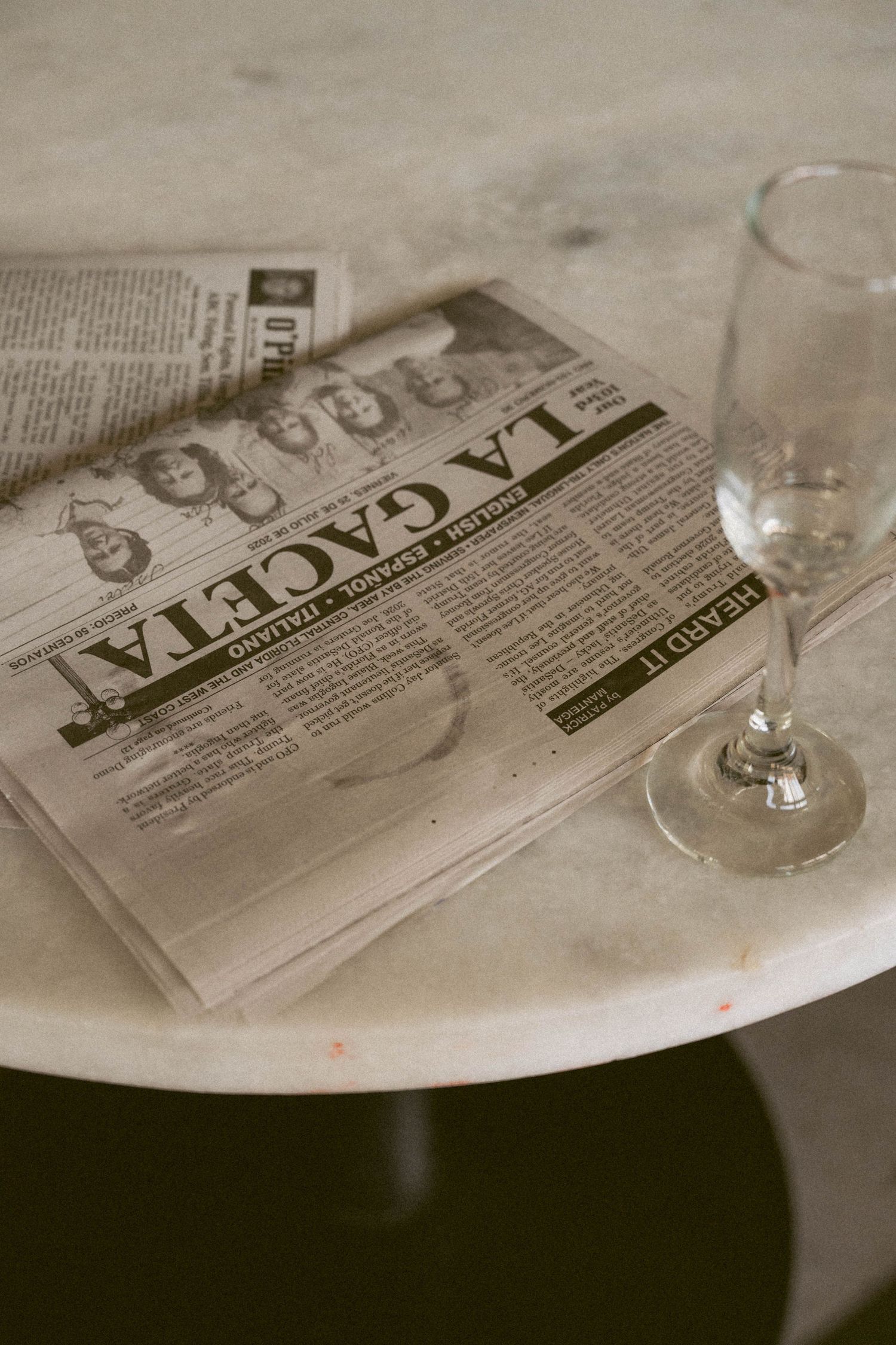 Vintage-style newspapers laid out on a white surface with wine glasses creating a nostalgic table setting.