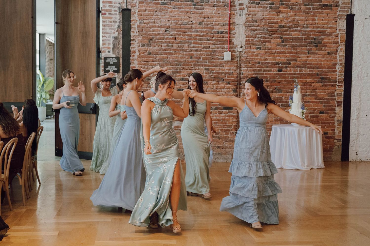 Wedding party in light blue dresses dancing and celebrating together on a wooden dance floor.