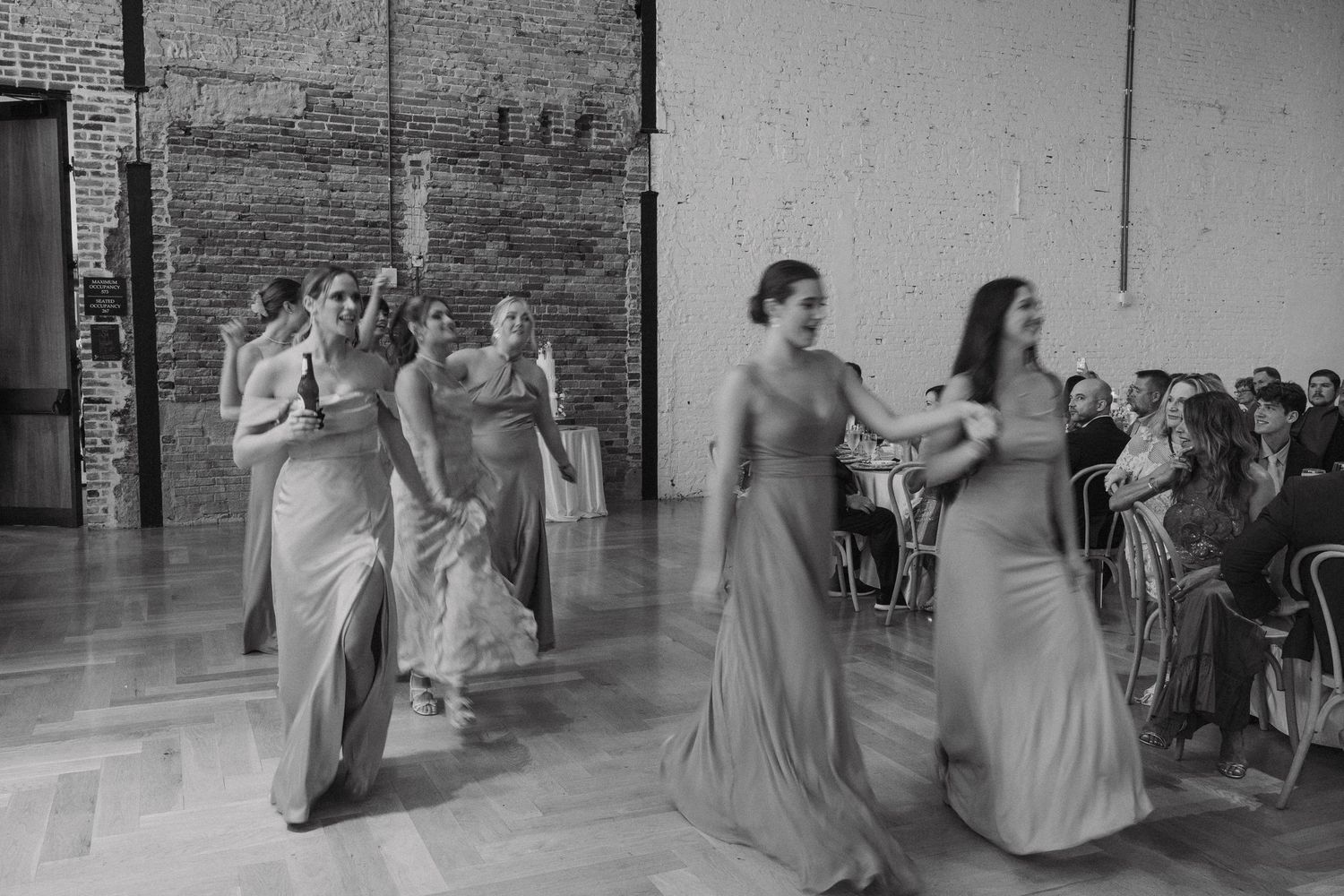 Wedding party poses in black and white photograph inside a spacious industrial venue.