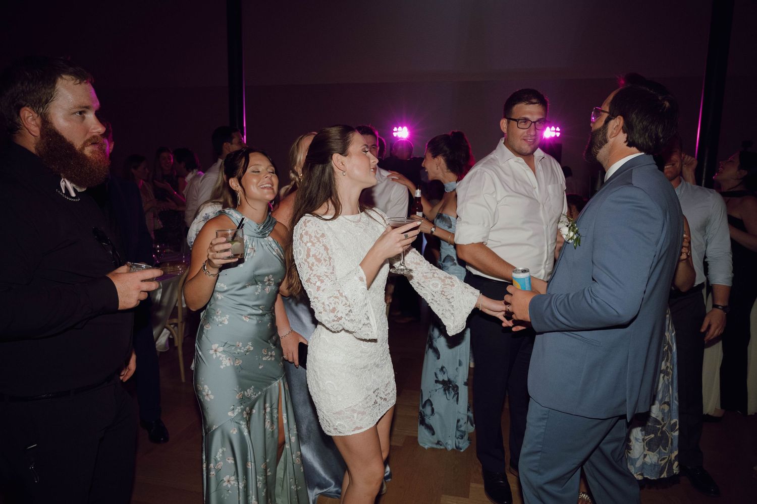 People dancing together at a dimly lit wedding reception with purple lighting and festive atmosphere.