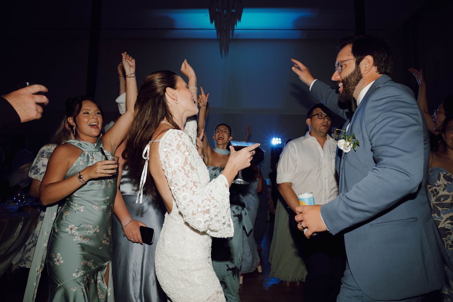 Wedding guests dancing together on a dark dance floor with blue lighting at a reception celebration.