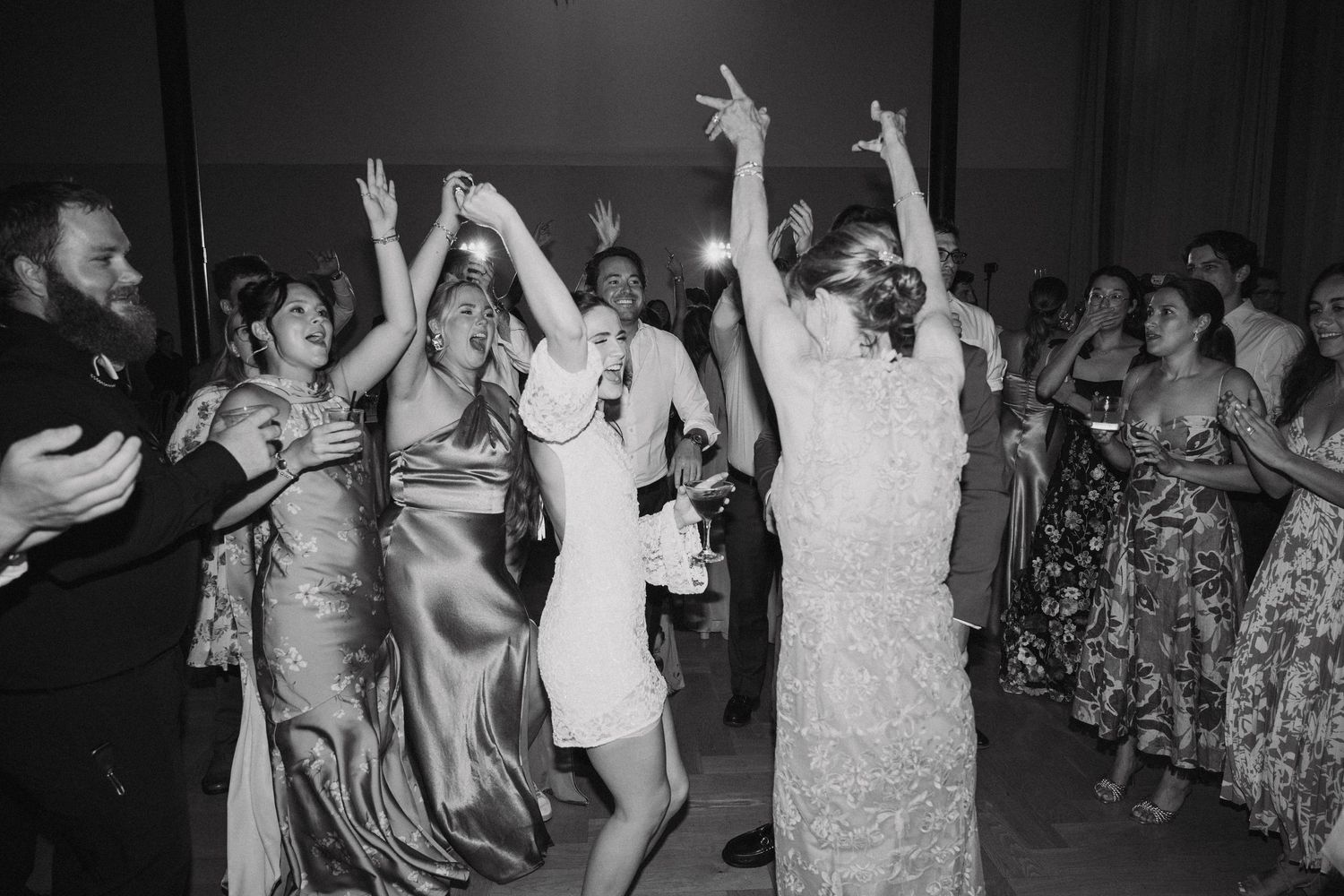 Black and white photo of wedding guests dancing and celebrating on a dance floor at a reception party.