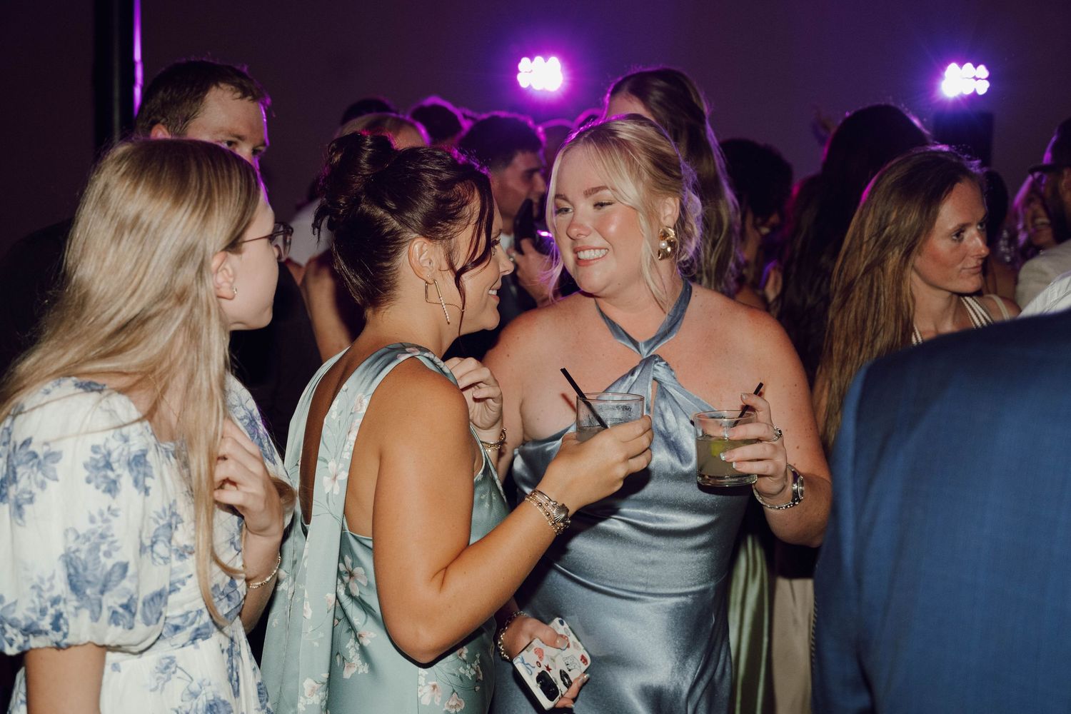 Party guests engaged in animated conversation while holding drinks at a dimly lit nighttime celebration.