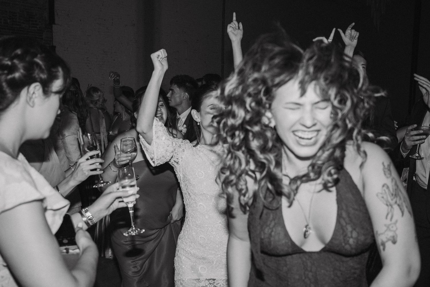 Black and white photo of wedding guests dancing and celebrating at a lively reception party.
