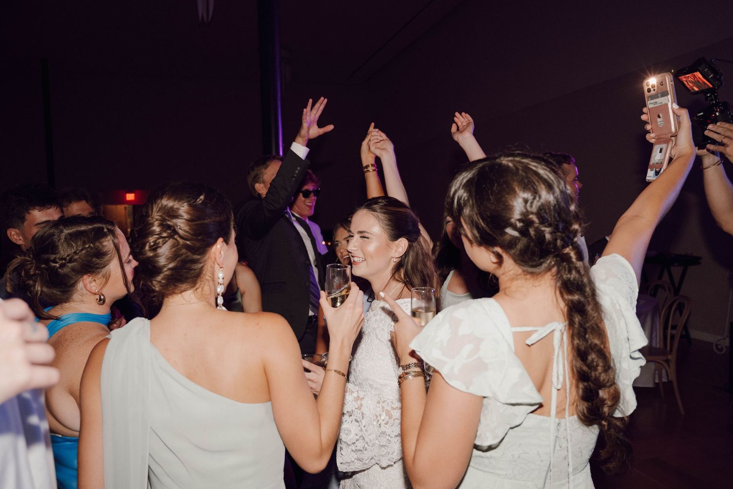 Wedding guests dance and celebrate on a dimly lit dance floor during an evening reception celebration.