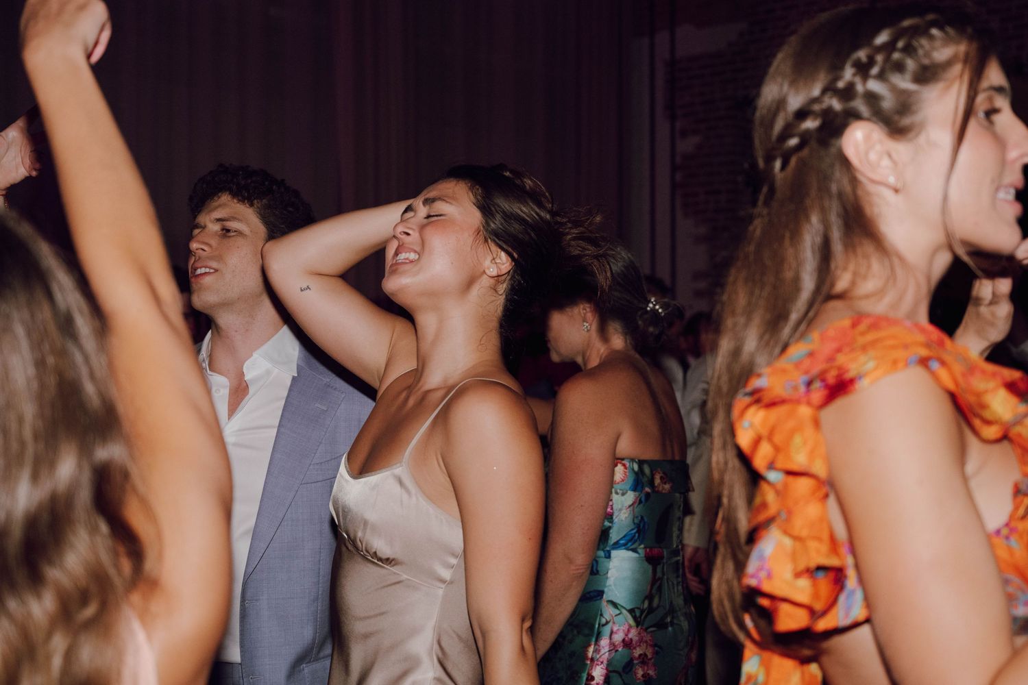 Crowd of people dancing and celebrating with hands raised at a lively indoor party event.