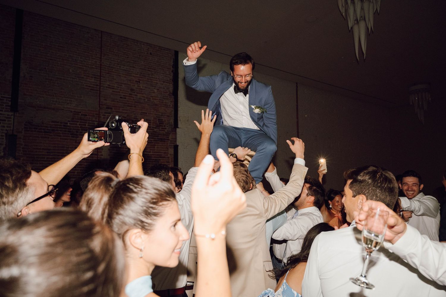 People dancing and celebrating at a lively wedding reception with hands raised in the air on a crowded dance floor.