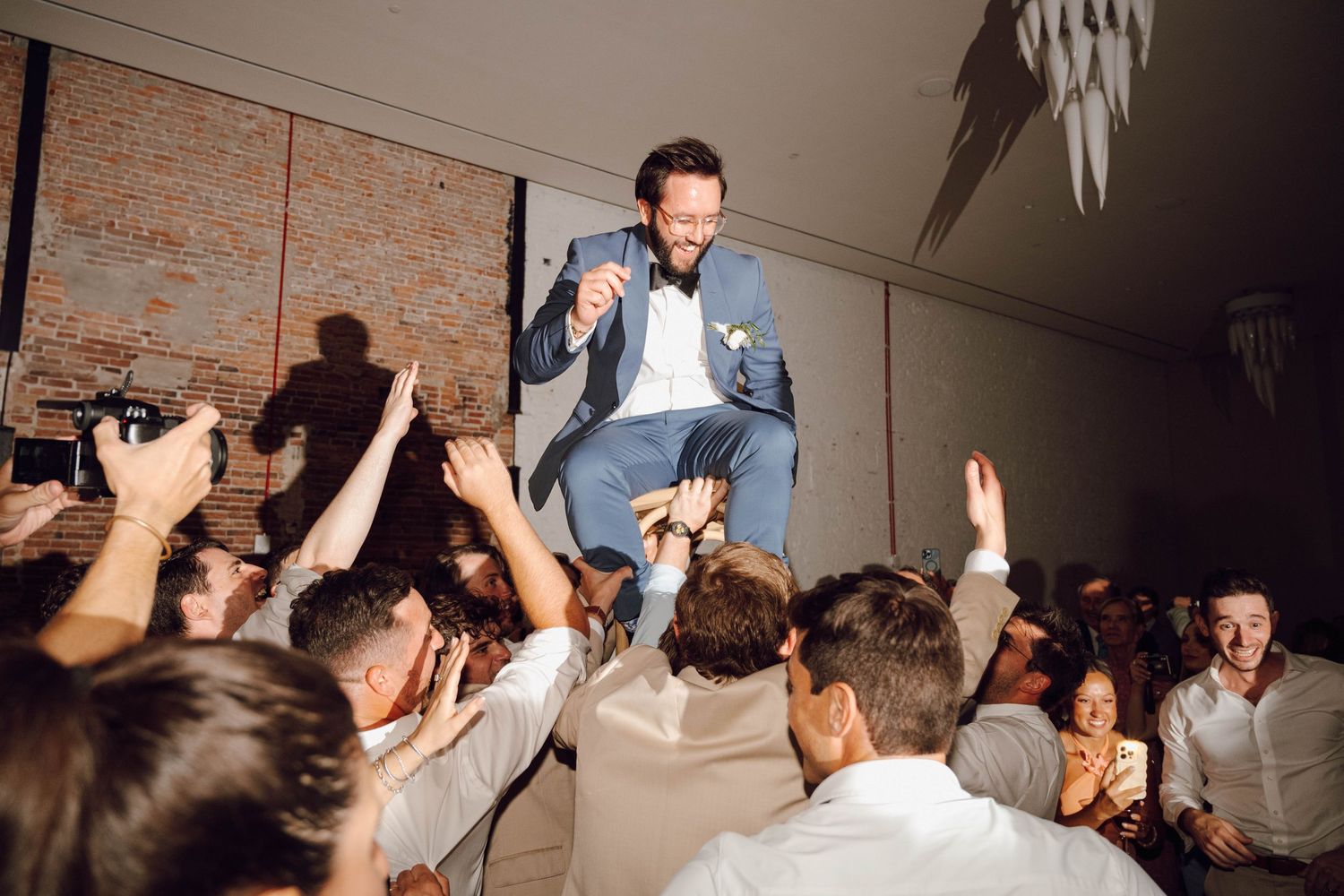 Energetic crowd dancing and celebrating with raised arms at a wedding reception party on the dance floor.