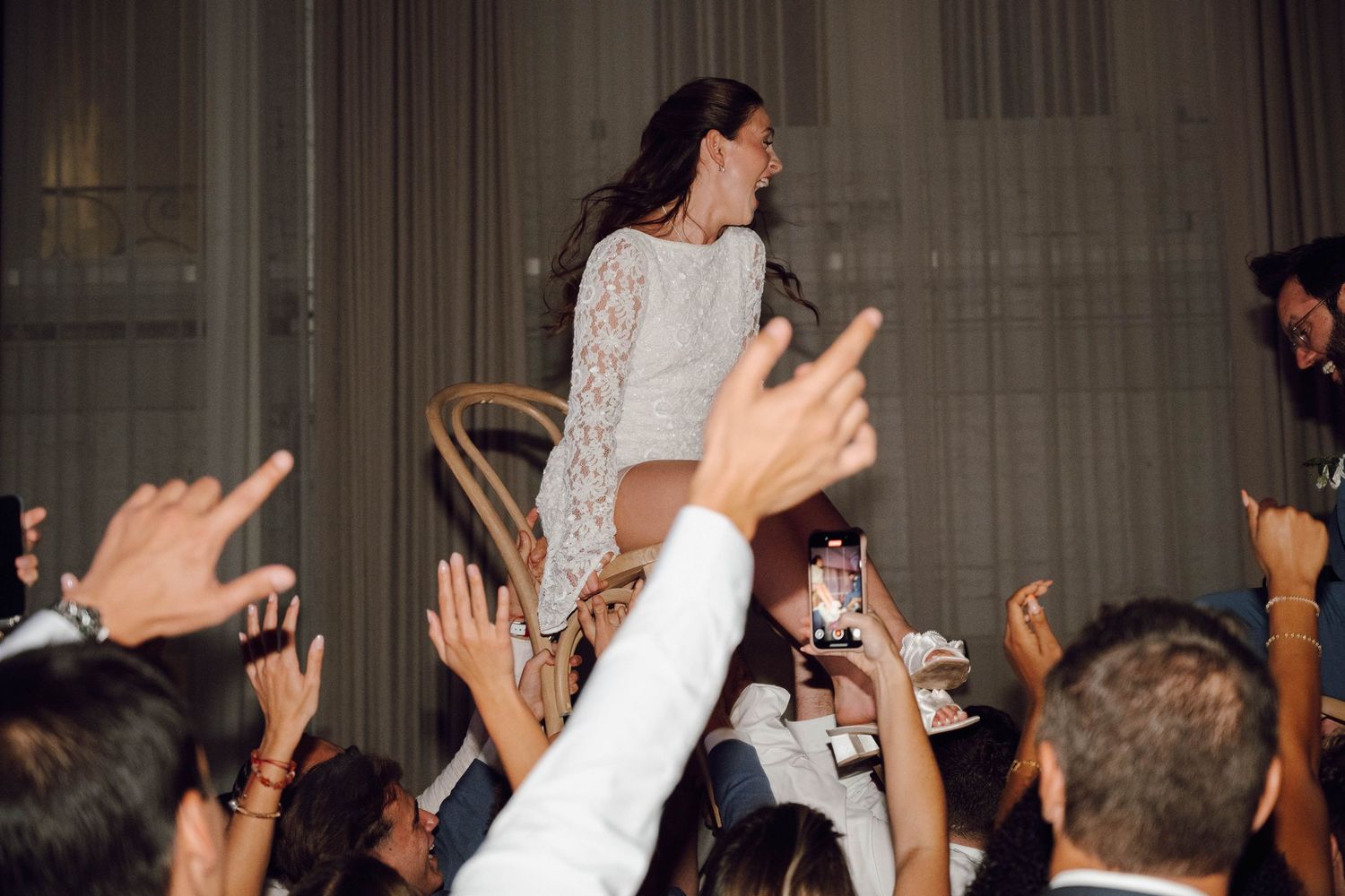 People dancing with hands up in the air at an indoor celebration venue.