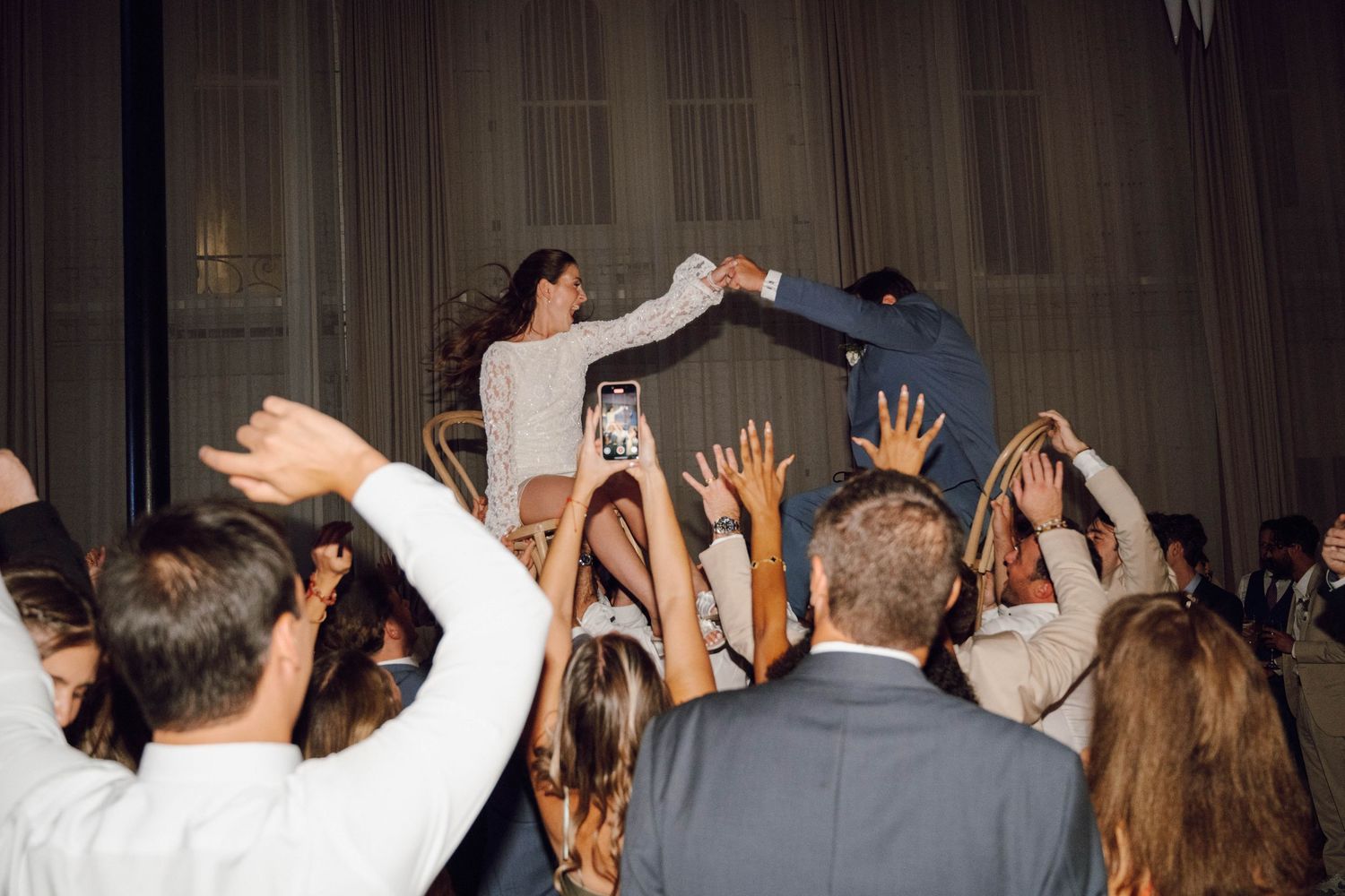 A crowd of people dancing with their hands raised at a lively indoor party or celebration.