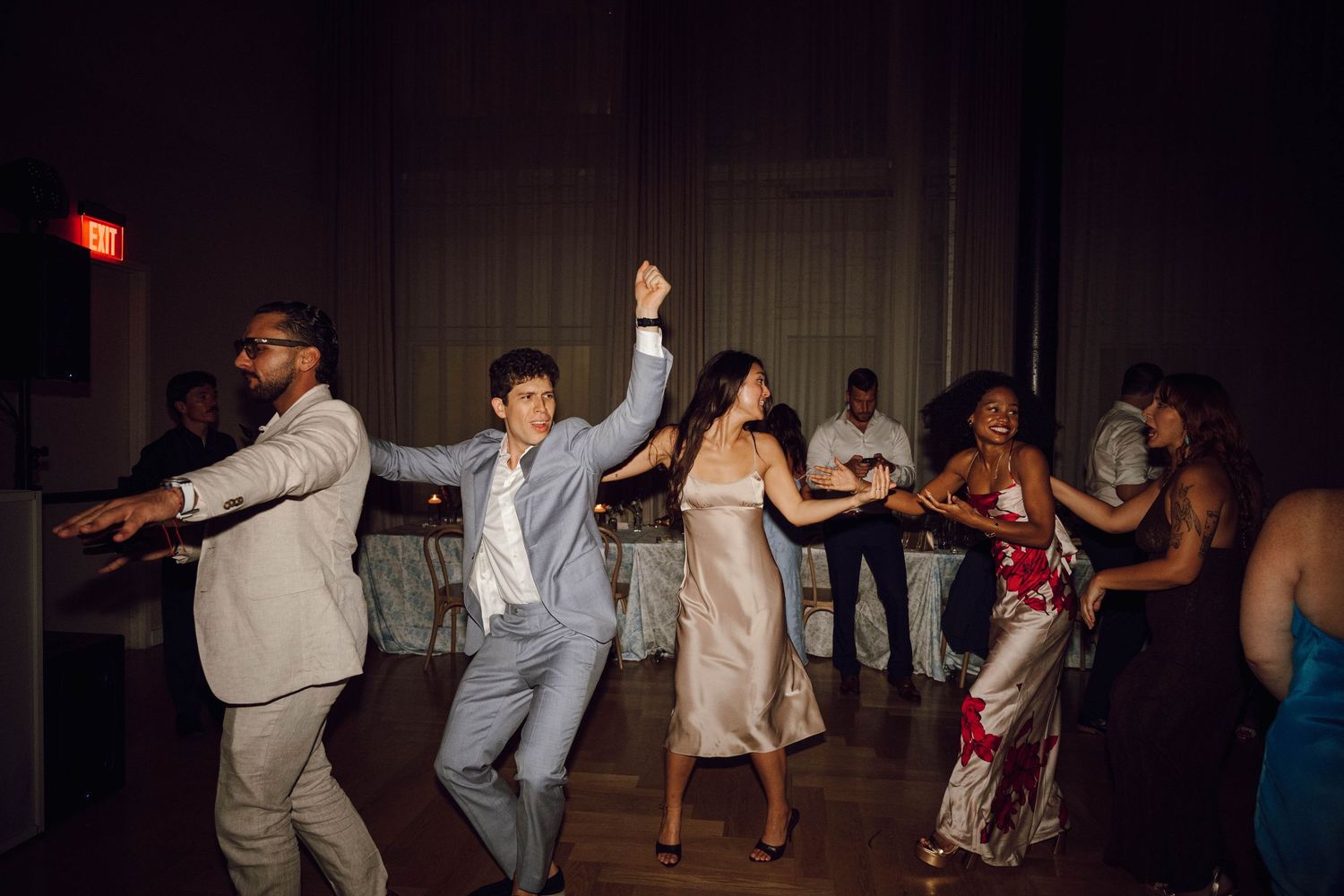 Wedding party dancing in a line formation on a dimly lit dance floor.