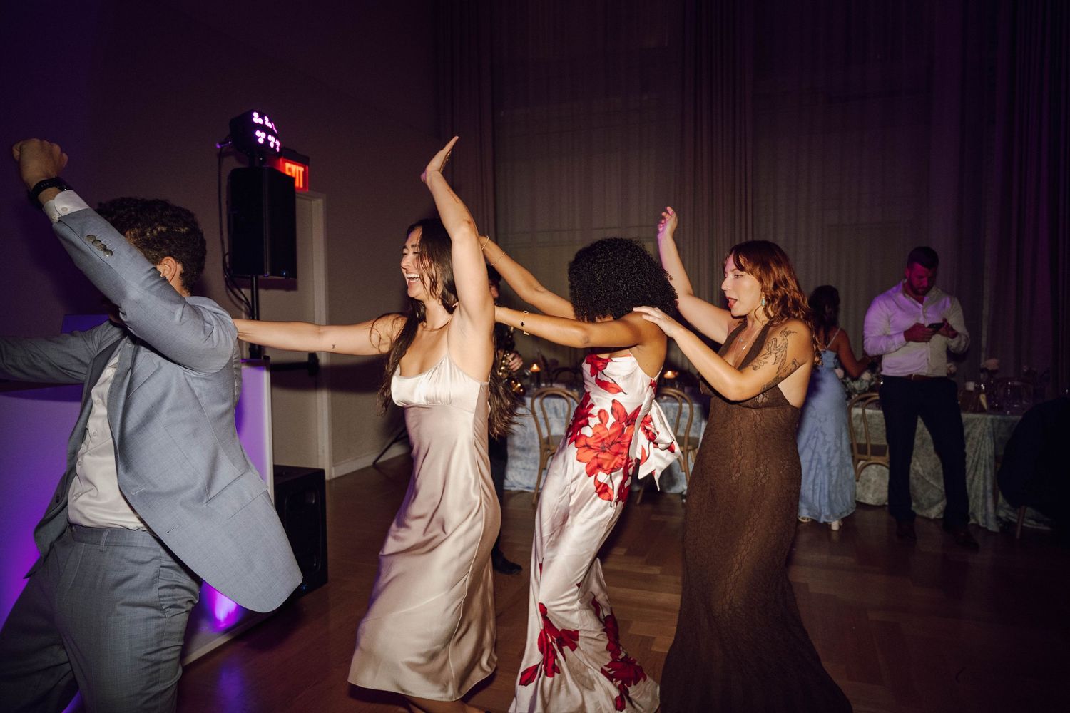 People dancing and celebrating on a dark dance floor with purple lighting during a wedding reception party.