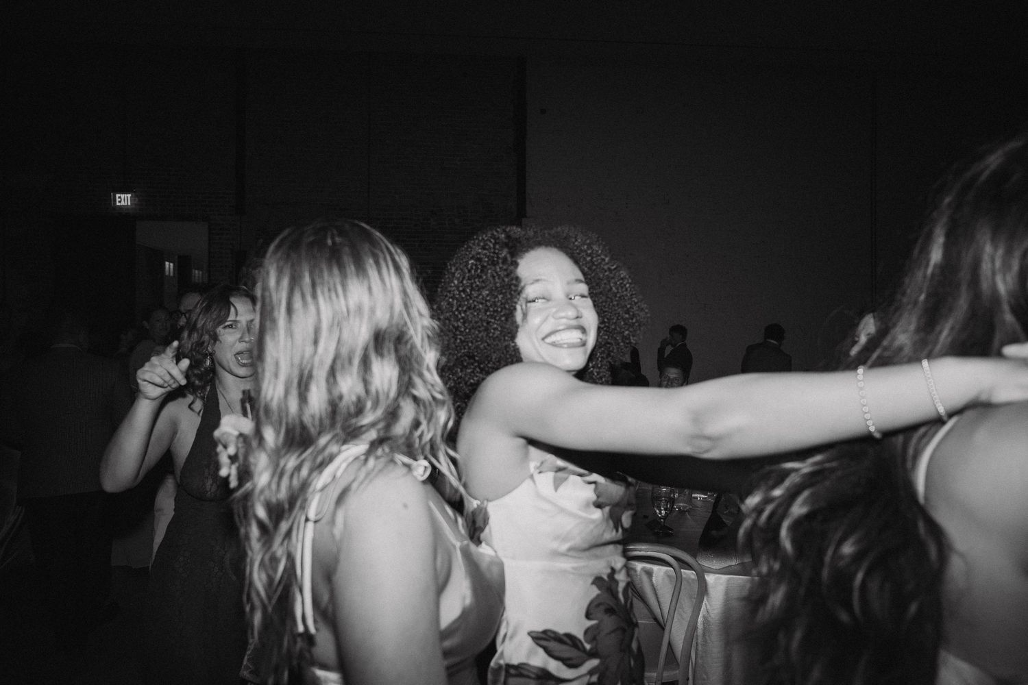Dark silhouettes of party attendees dancing with arms raised against a black background.