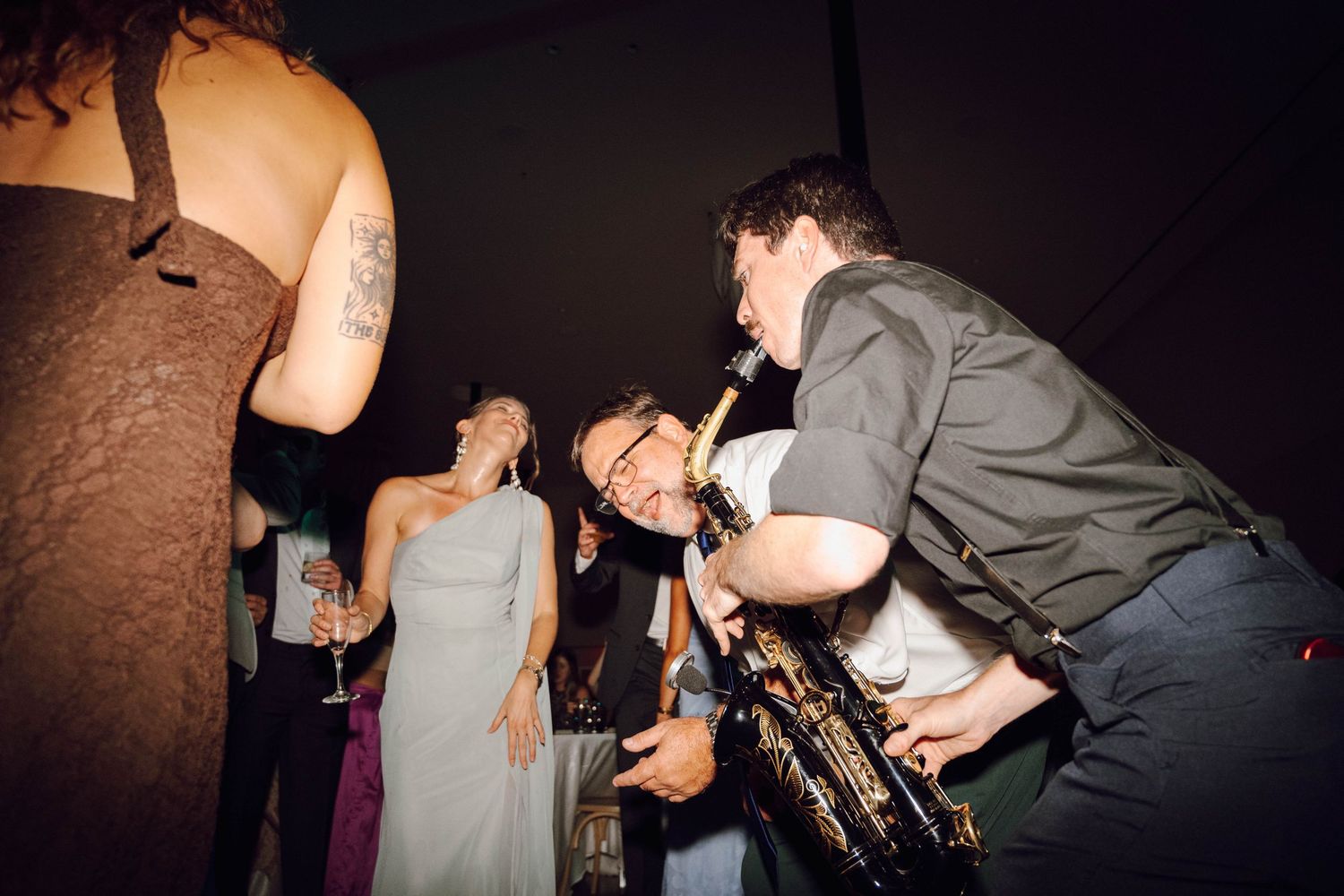 Party guests dancing energetically at a wedding reception in dark lighting.