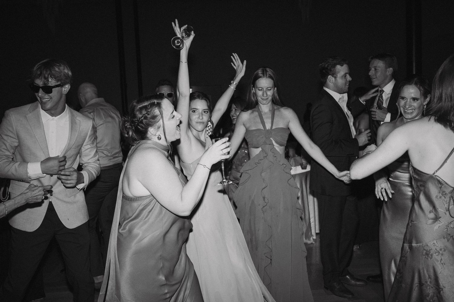 People dancing and celebrating at a formal event with raised arms and elegant dresses.