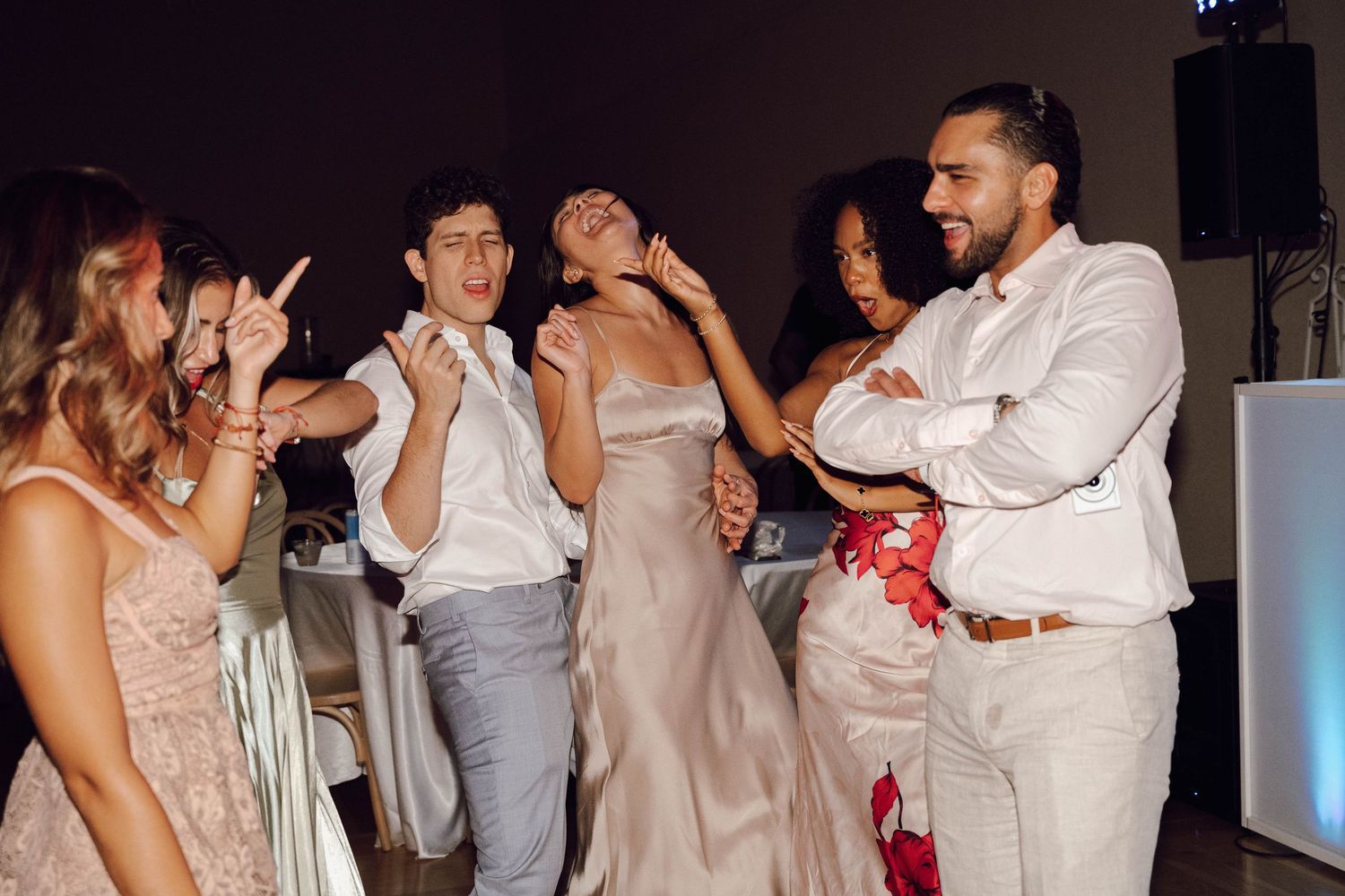 Wedding party members dance and celebrate together on a dark dance floor with atmospheric lighting.
