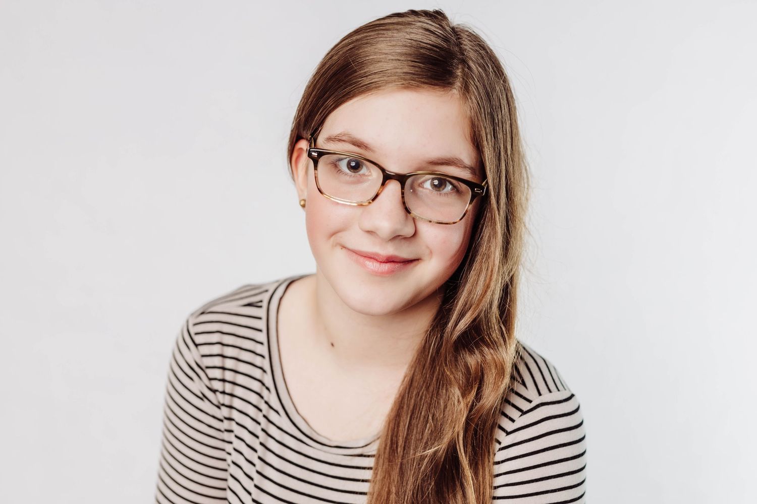 A person wearing glasses and a striped shirt smiles warmly at the camera against a white background.