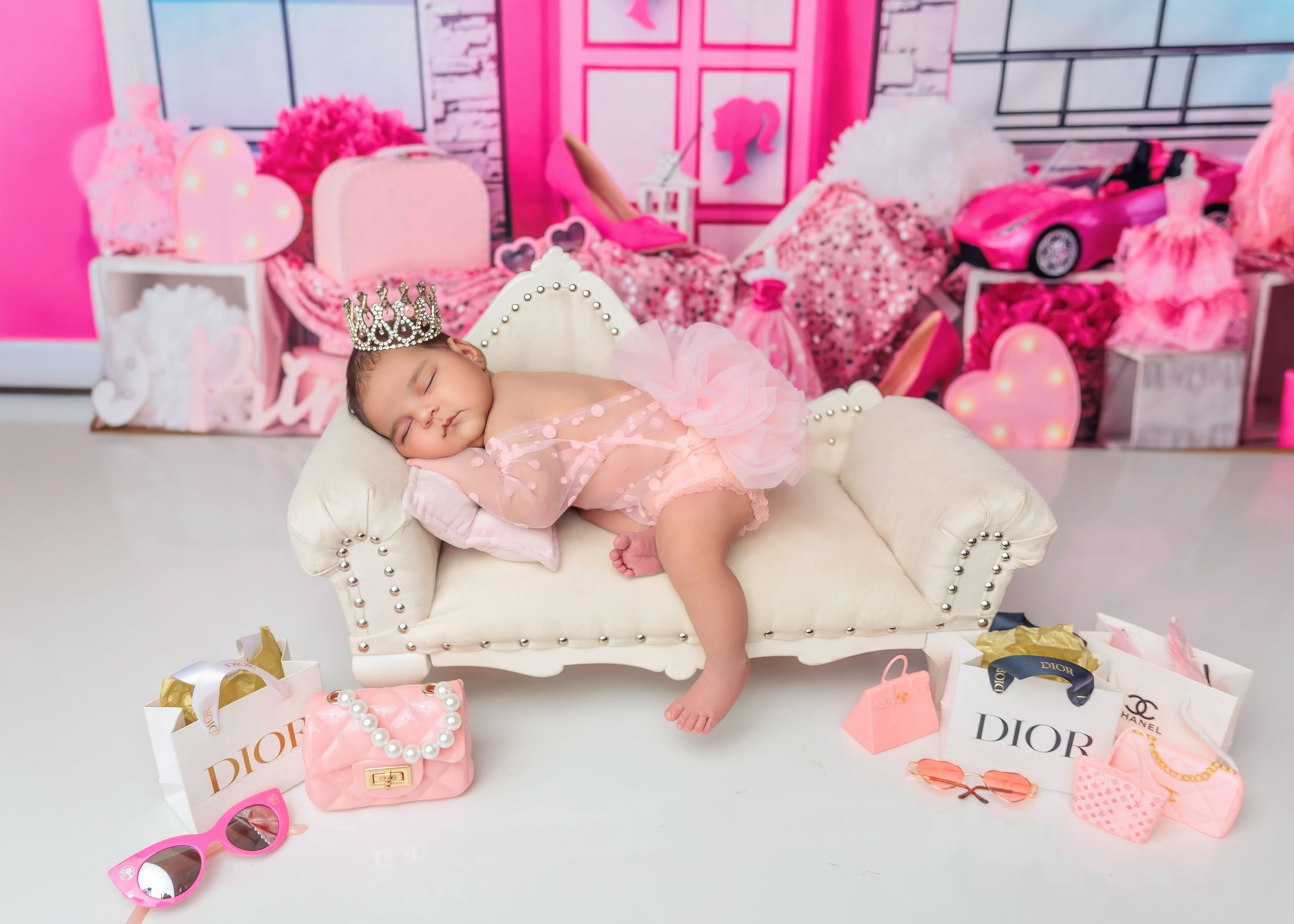 Sleeping newborn in pink tutu on mini couch with Dior accessories Barbie theme.