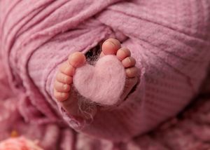 Tiny newborn baby feet with pink felt heart between toes on soft pink knit blanket.