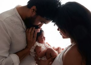 Parents tenderly gazing at their newborn baby dressed in white in a soft lit portrait.