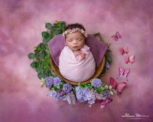Sleeping newborn baby wrapped in purple swaddle in bowl with butterflies and flowers.
