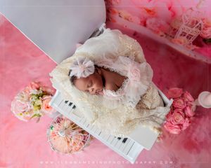 Aerial view of newborn baby in lace outfit sleeping on a white toy piano with pink roses.