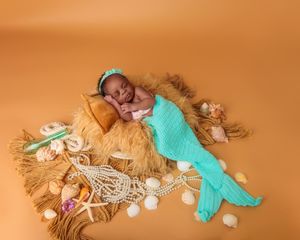 Newborn baby posed as a mermaid with teal tail on a rustic net with seashells and pearls.
