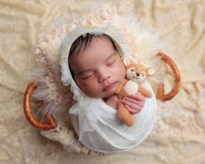 Sleeping newborn baby wrapped in white swaddle wearing a floral bonnet and holding a fox stuffed animal.