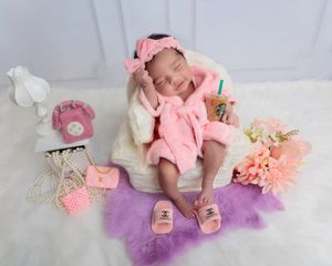 Newborn baby girl in pink bunny robe posed in a styled Chanel and Starbucks themed photography setup.