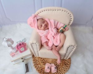Newborn baby in pink Chanel outfit sleeping in a cream armchair with luxury brand accessories.