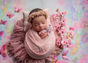 Sleeping newborn baby wrapped in pink with floral crown surrounded by cherry blossoms and butterflies.