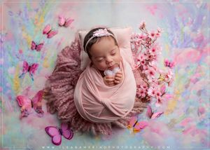 Sleeping newborn baby wrapped in pink swaddle surrounded by butterflies and cherry blossoms in studio.