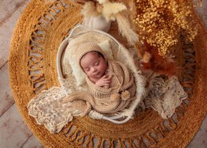 Sleeping newborn baby in cream knit wrap and bonnet in a basket with golden boho decor.