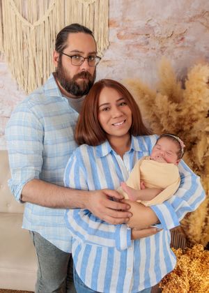 Happy couple smiling and holding their newborn baby in a boho-themed professional photography studio.