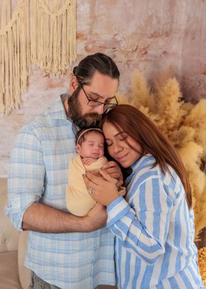 New parents tenderly holding their swaddled newborn baby together in a boho-styled photography studio.