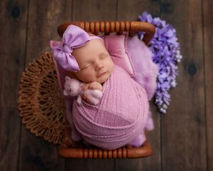 Sleeping newborn baby girl swaddled in purple wrap with bow headband in wooden basket.