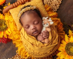 Newborn baby wrapped in mustard yellow with sunflowers and a giraffe toy in autumn setting.