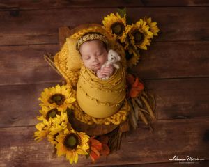 Sleeping newborn baby swaddled in yellow wrap with sunflowers and white teddy bear.