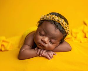 Peaceful newborn baby sleeping on yellow blanket wearing a golden floral headband.