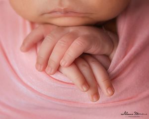 Macro close-up of delicate newborn baby fingers and tiny hands resting on soft pink fabric wrap.