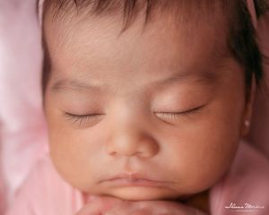 Close-up portrait of peaceful sleeping newborn baby girl with tiny pearl earrings on soft pink background.