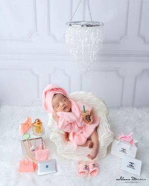 Newborn baby girl in pink robe posed with miniature Chanel bags and Starbucks props.
