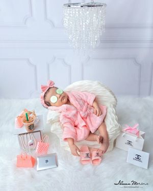 Newborn baby girl in pink spa robe with cucumber eye slices and Chanel props.