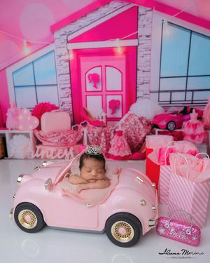 Sleeping newborn baby girl in pink car with Barbie themed backdrop and decorations.
