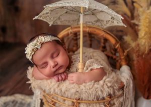 Peaceful newborn baby sleeping in rattan basket under decorative lace umbrella prop.