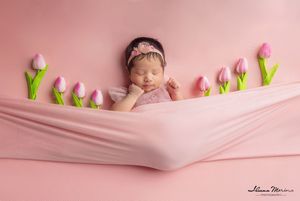 Sleeping newborn baby girl in pink wrap surrounded by tulips on pink background.