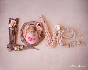 Newborn baby in pink swaddle posed inside letter O spelling LOVE with floral fabric letters on pink backdrop.