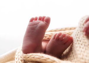 Close-up of tiny newborn baby feet peeking out from soft cream knitted blanket.