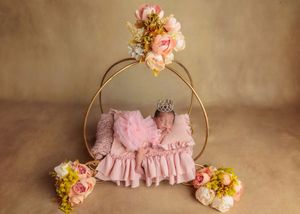 Newborn baby in pink tutu with crown sleeping on miniature bed with floral arch.