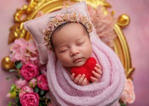Sleeping newborn in lavender wrap holding red heart inside gold ornate frame with roses.